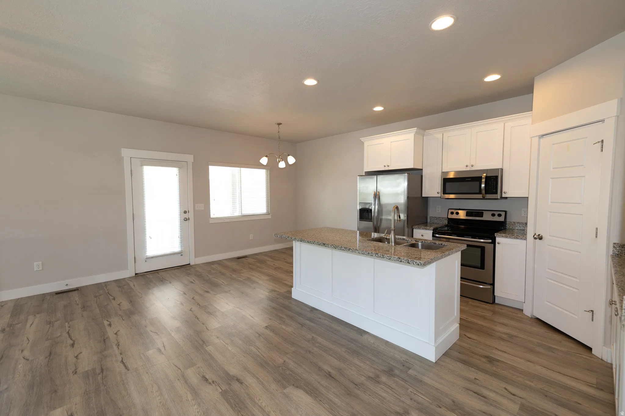 Open-concept living space featuring wood-finish flooring, a contemporary kitchen island with granite countertop, stainless steel appliances, white cabinetry, and recessed lighting