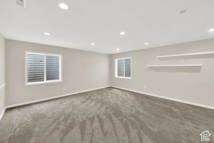 Spacious room featuring neutral wall paint, recessed lighting, two windows, and textured carpet flooring