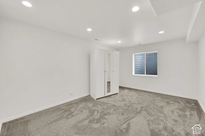 Spacious room featuring neutral carpeting, a white window frame, and recessed lighting