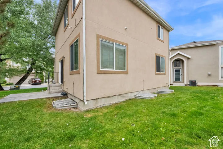 Rear exterior featuring stucco siding, multiple windows with blinds, a concrete patio, and a grass lawn