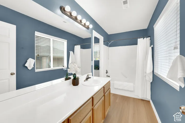 Bathroom featuring a single vanity with a white countertop and wood-finish cabinetry, a large mirror, and a white tub and shower combination