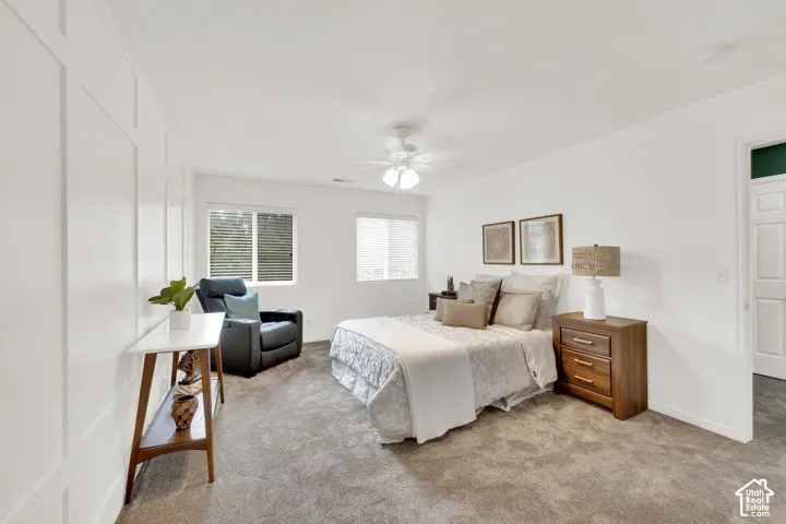 Carpeted bedroom with a paneled accent wall, dual windows with blinds, a ceiling fan, and a paneled interior door