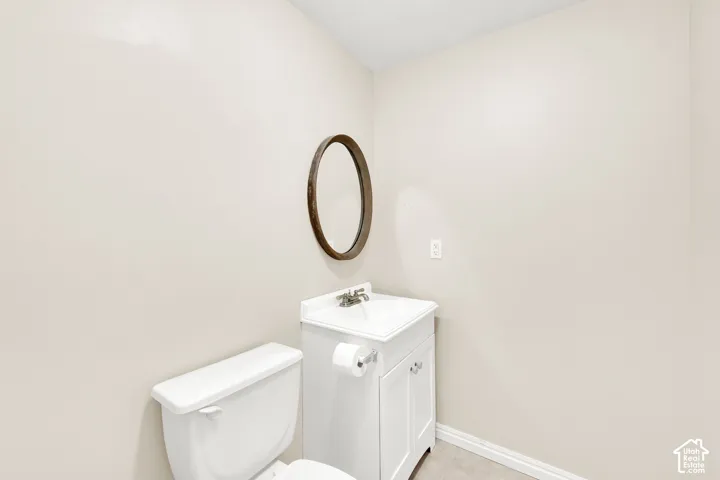 Powder room featuring a white toilet, a white vanity with an integrated sink, and an oval-framed mirror