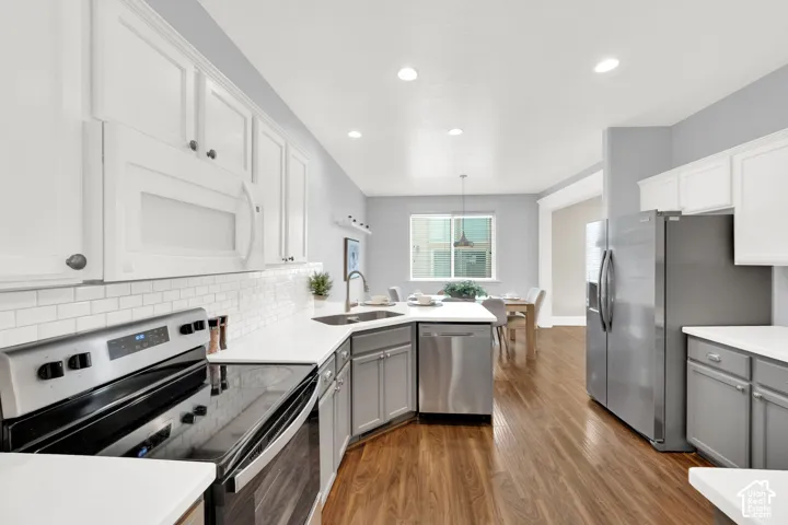 Modern kitchen featuring white upper cabinetry, gray lower cabinetry, stainless steel appliances, wood-finish flooring, and white countertops