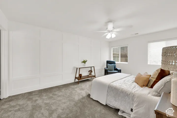 Bedroom featuring a paneled accent wall, neutral carpeting, and a ceiling fan