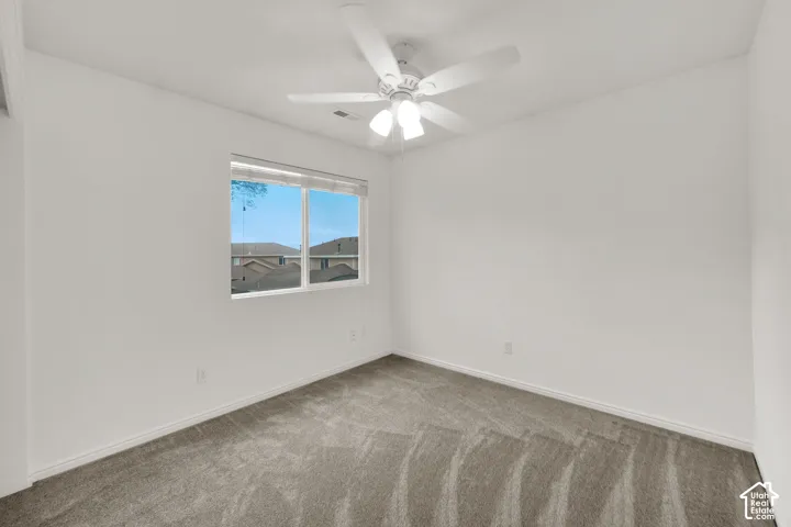 Room featuring a window with natural light, grey carpet flooring, white walls, white baseboards, and a ceiling fan with integrated lighting
