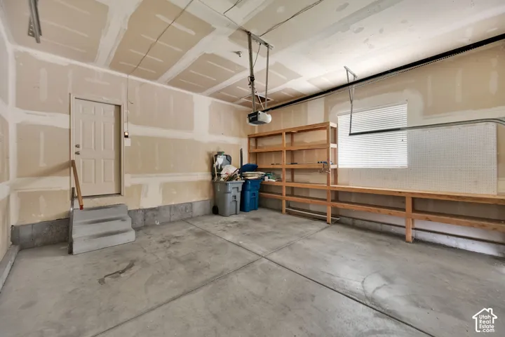 Spacious garage featuring a concrete floor, built-in shelving, an overhead door opener, a window with blinds, and a side access door
