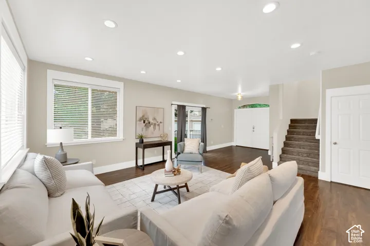 Spacious living area featuring wood-finish flooring, recessed lighting, white trim, and a carpeted staircase