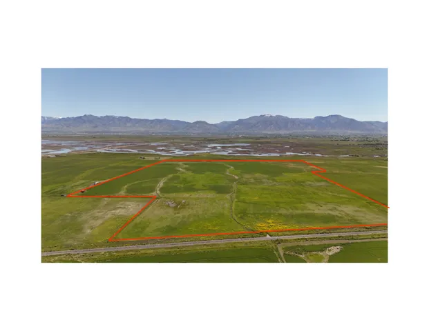 Expansive agricultural land featuring a verdant field, visible waterways, and distant mountain ranges