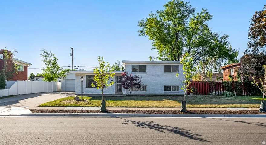 White painted brick exterior featuring a single-car garage, concrete driveway, and a fenced backyard