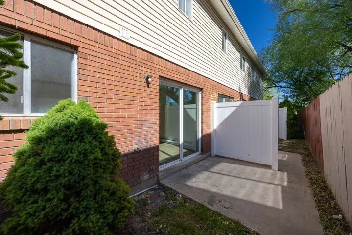 Rear patio with concrete surface, brick and siding exterior, sliding glass door, and a white privacy fence section