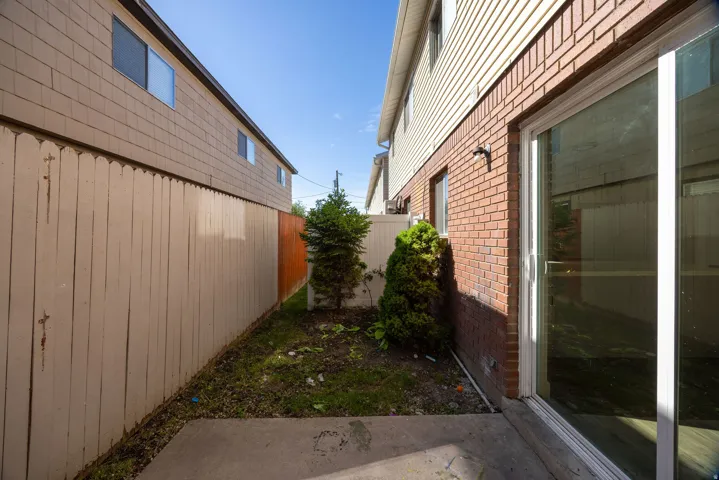 Concrete patio area with a sliding glass door entry, brick facade, and vinyl siding