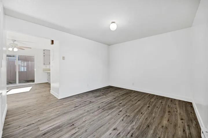 Spacious interior room featuring wood-finish flooring, white baseboards, and a neutral wall color