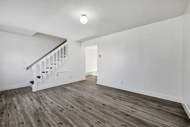 Spacious interior with wood-finish flooring, crisp white walls, and a recessed storage area beneath the staircase