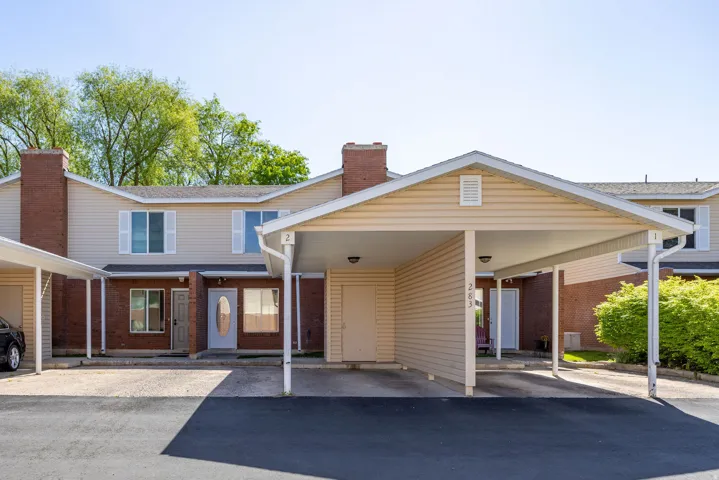 Townhome exterior featuring brick and siding finishes, individual carports, and mature landscaping