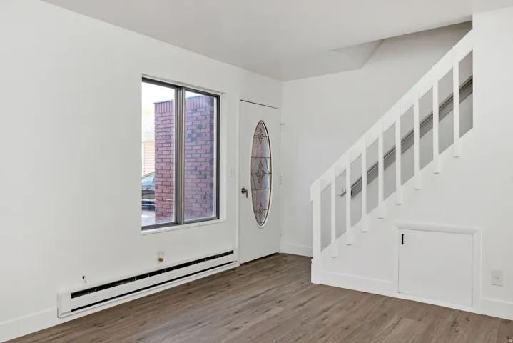 Entry area with wood-finish flooring, a white paneled door with an oval stained-glass insert, and a white staircase with spindle railing