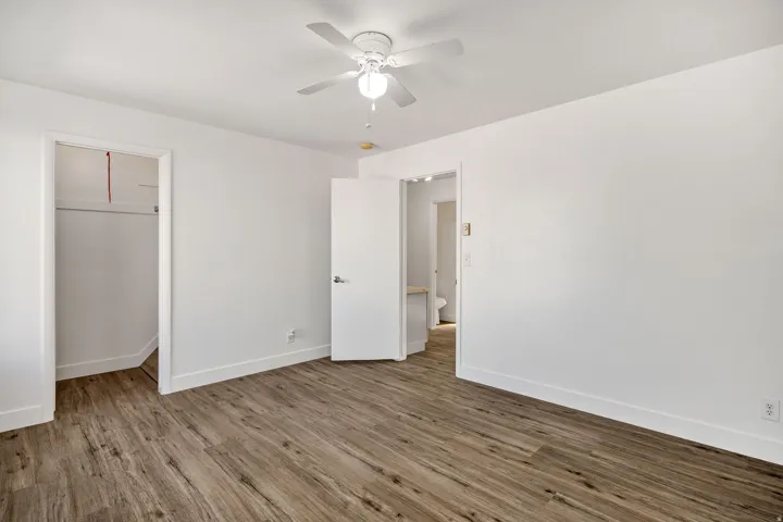Spacious room featuring wood-finish flooring, white walls, and a ceiling fan