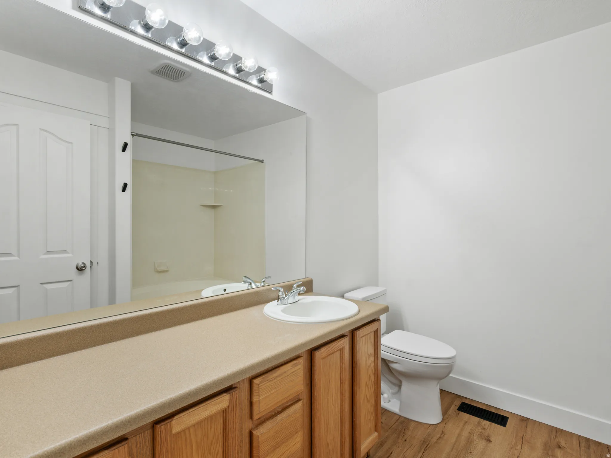 Bathroom featuring a wood-finish vanity with a light-toned countertop, an integrated sink with chrome faucet, and a large wall-mounted mirror