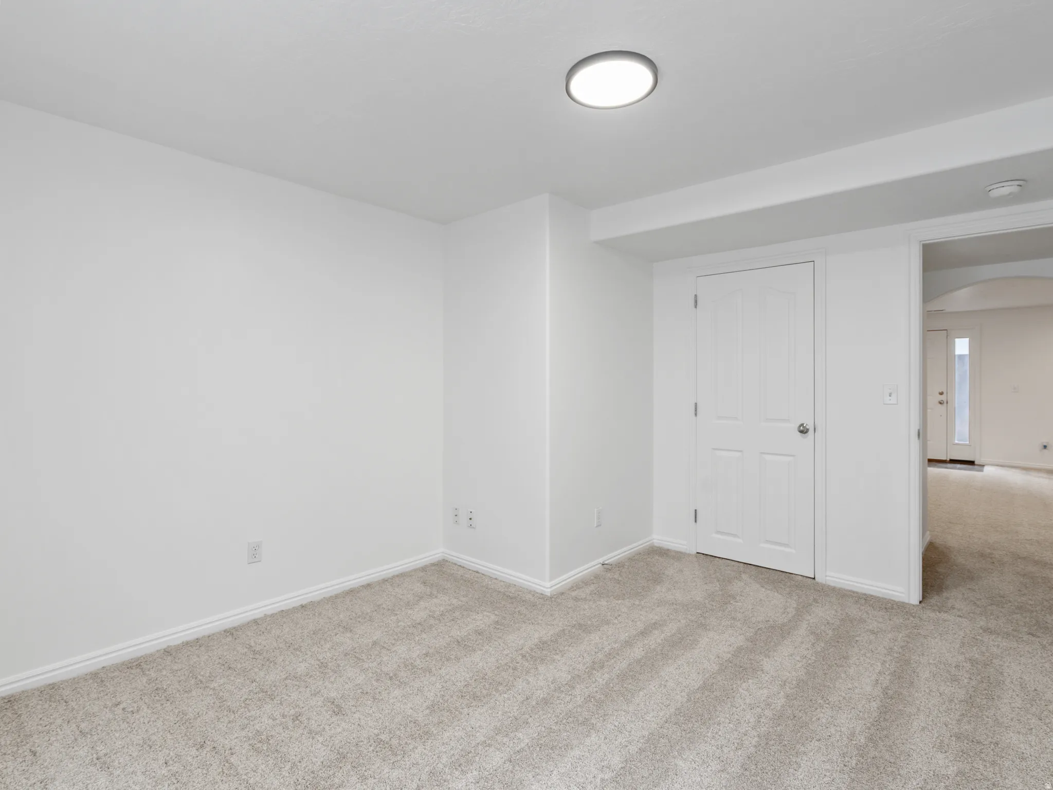 Neutral tone-on-tone carpet flooring extending throughout, white baseboards, and a flush-mount ceiling light fixture