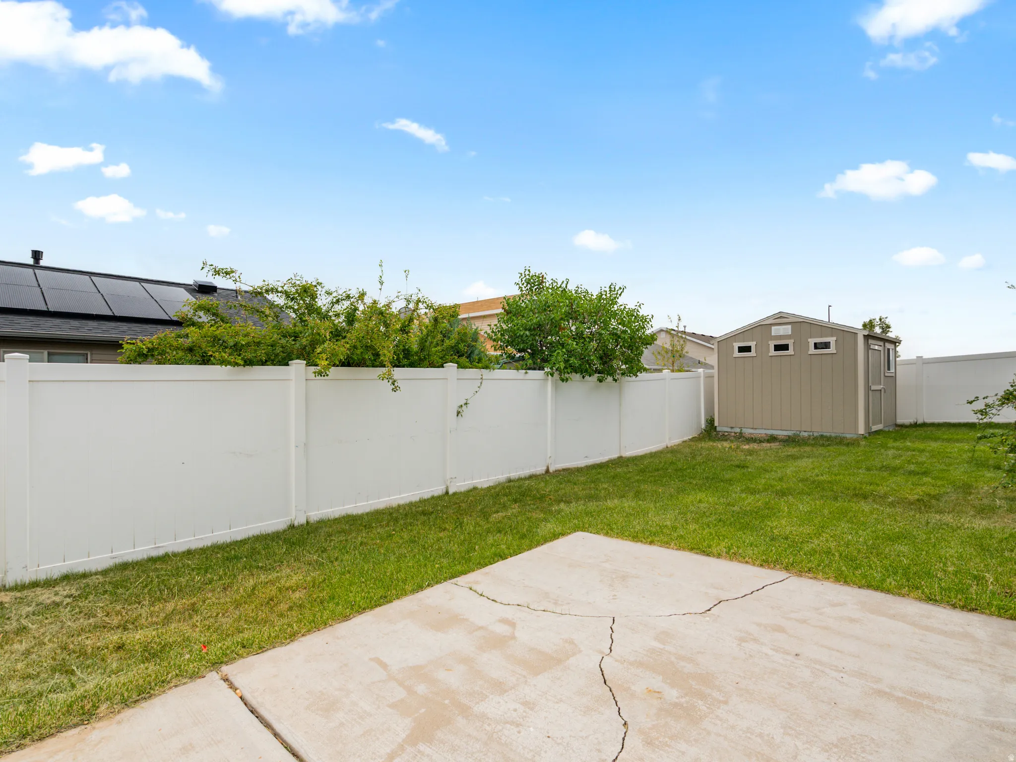 Expansive backyard featuring a lush lawn, white privacy fencing, and a detached storage shed