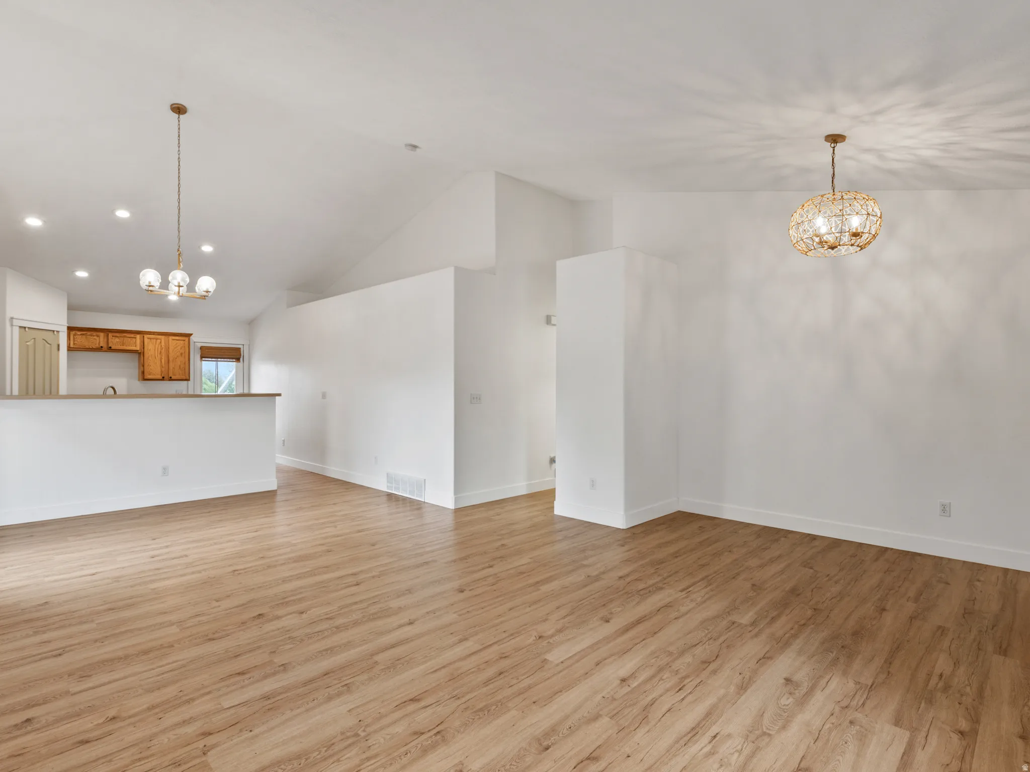 Open-concept living area featuring wood-finish flooring, vaulted ceilings, and a decorative orb chandelier