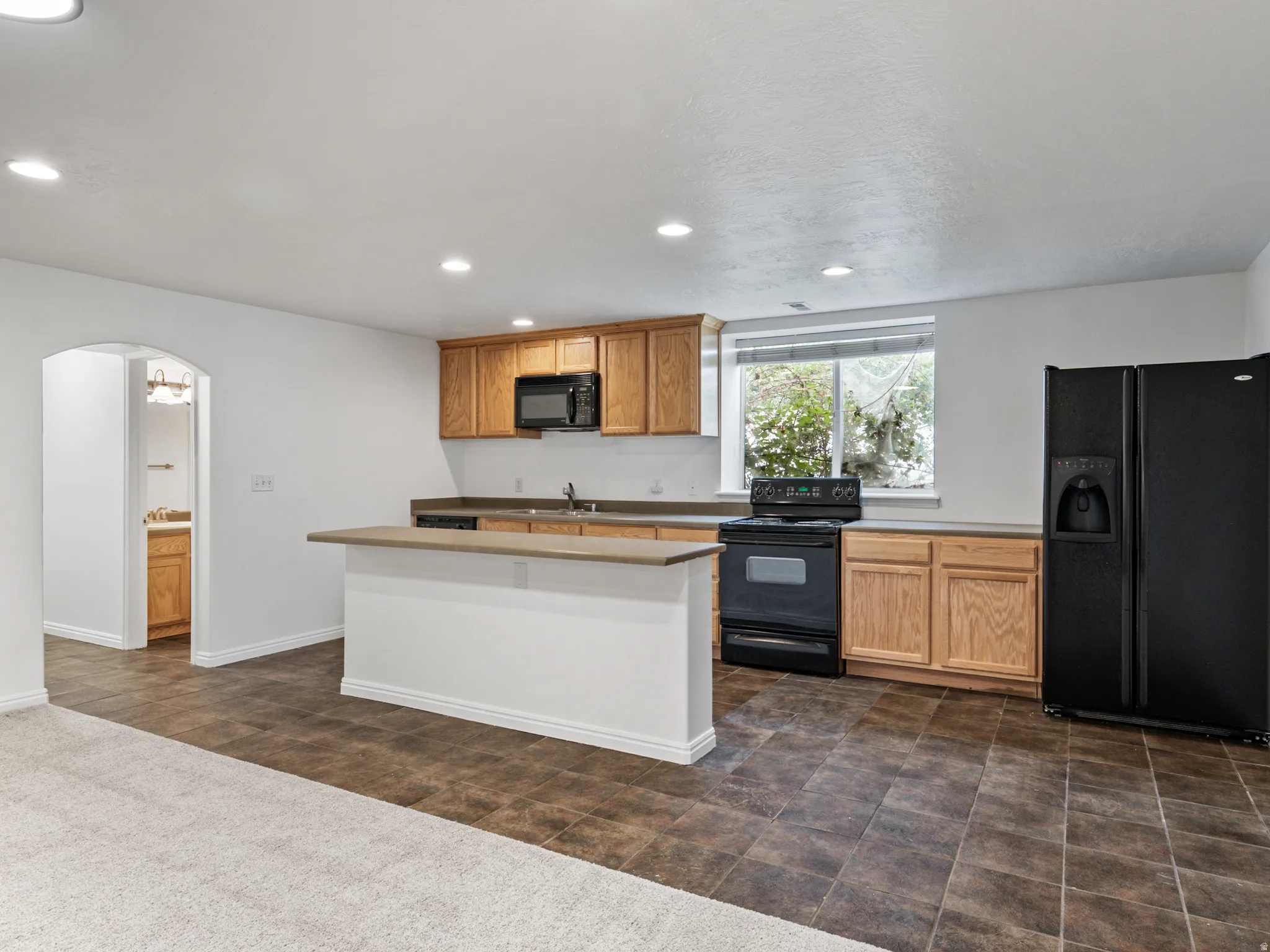 Kitchenette featuring oak-finish cabinetry, black appliances, solid surface countertops, and a breakfast bar island