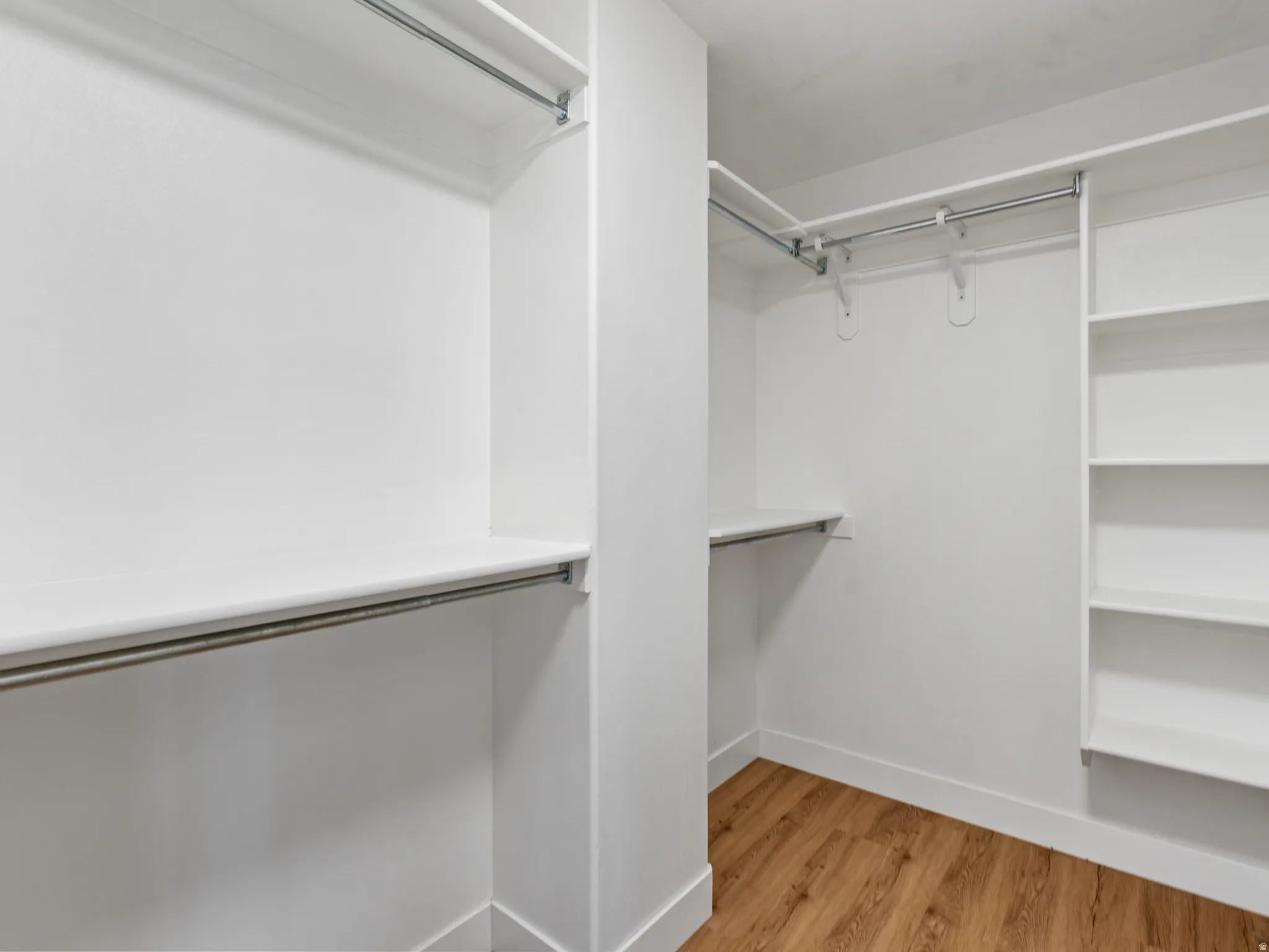 Walk-in closet featuring white built-in shelving, multiple hanging rods, and wood-finish flooring