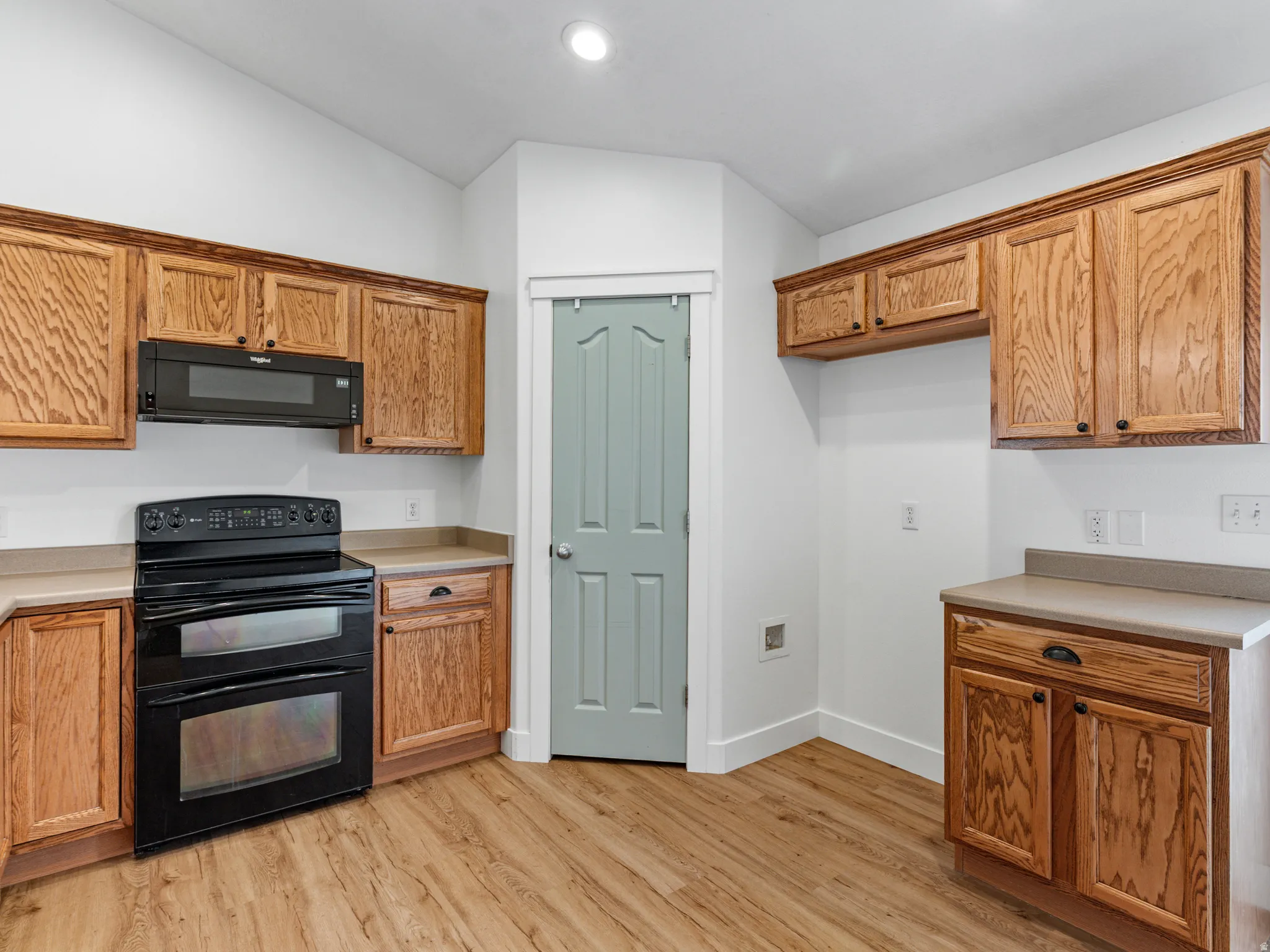 Kitchen featuring wood-finish flooring, light wood cabinetry with dark hardware, a double-oven range, an over-the-range microwave, and light-toned countertops