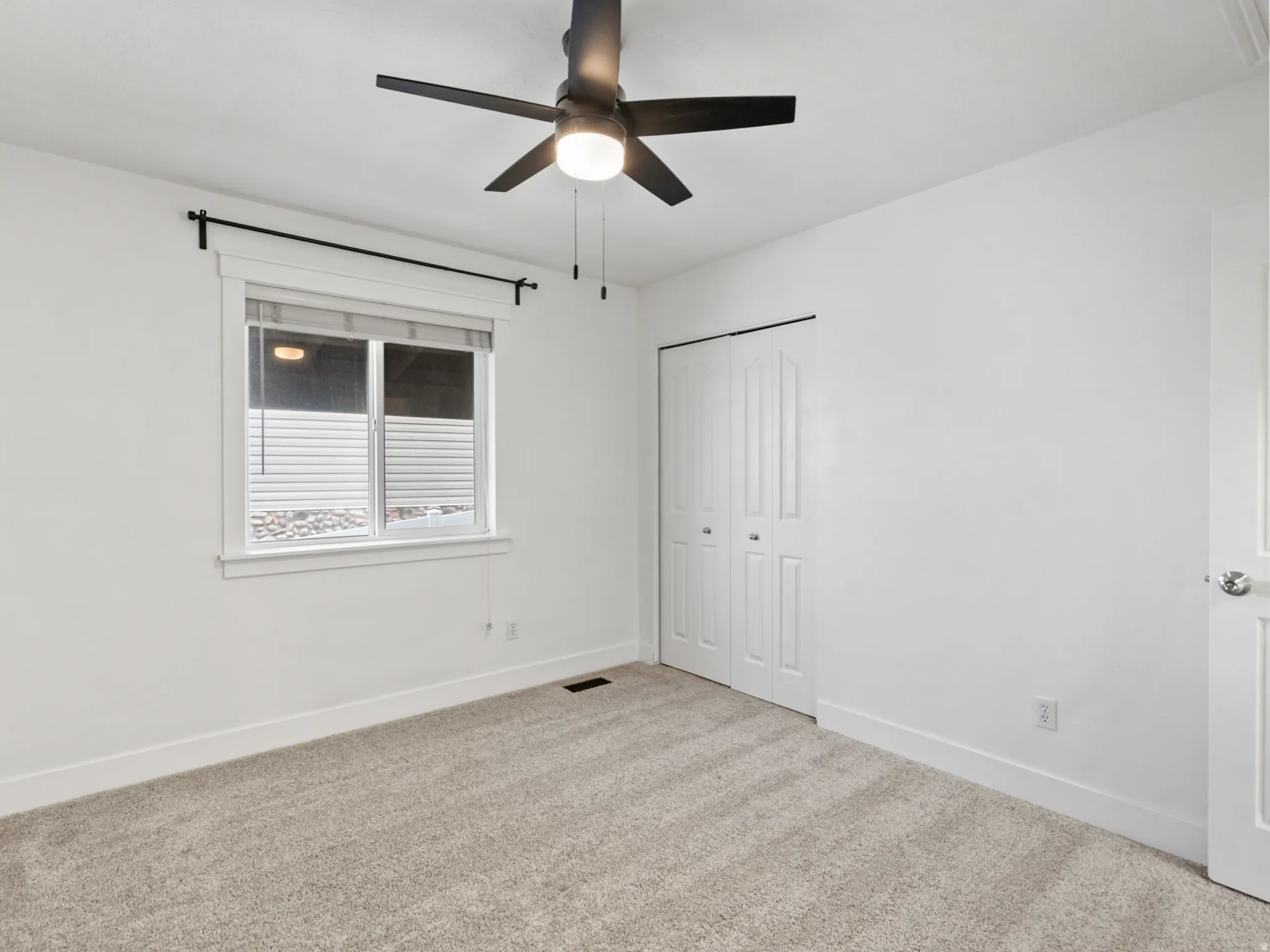 Carpeted room with a ceiling fan, white trim, and a double-door closet