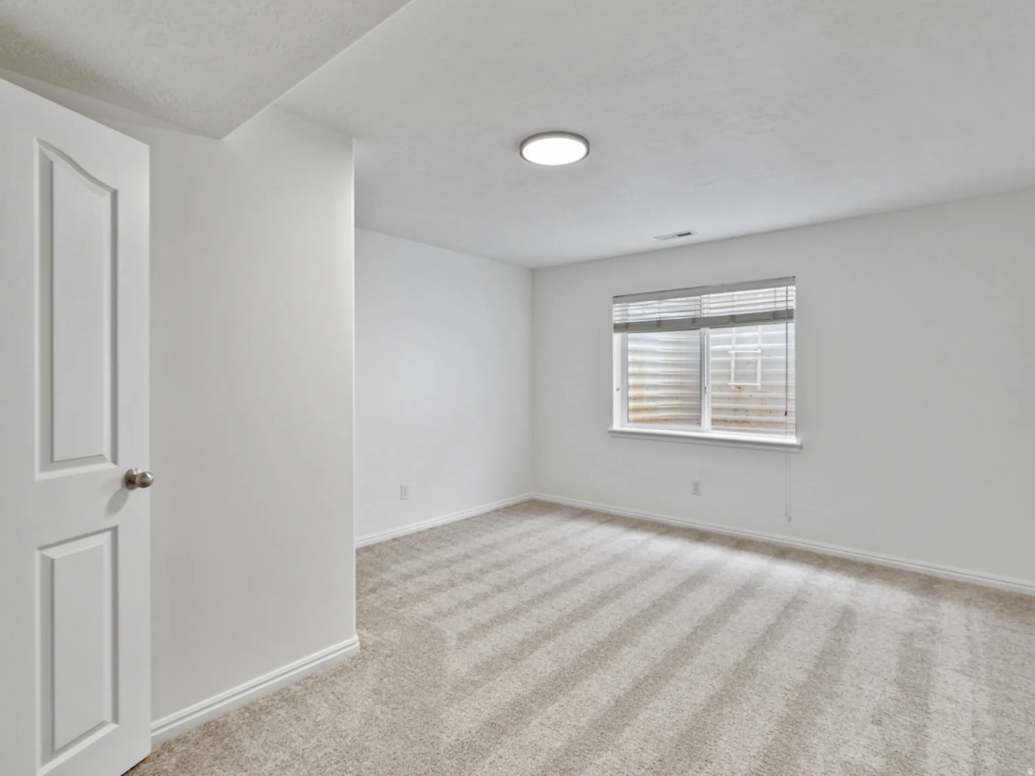 Light-colored carpeted flooring with a window featuring horizontal blinds