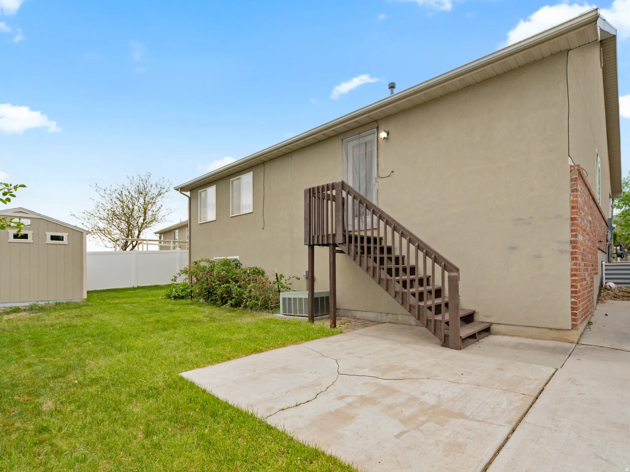 Rear exterior featuring stucco and brick siding, a ground-level concrete patio, and a wooden staircase leading to an upper-level entry