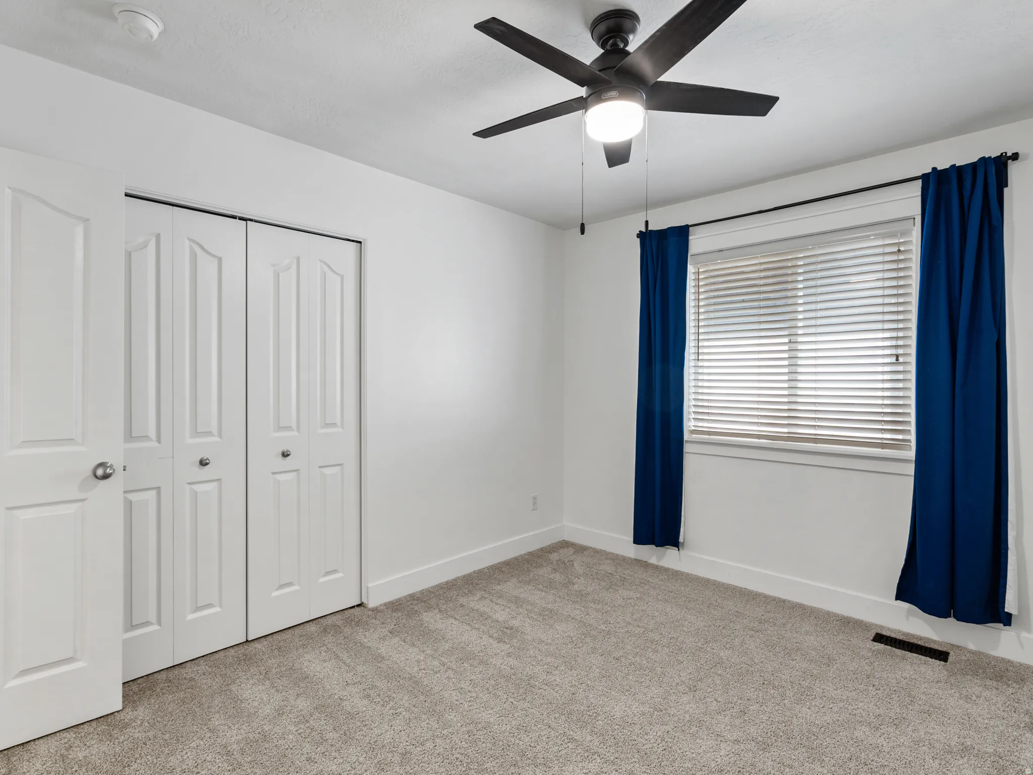 Bright interior room featuring a ceiling fan with integrated lighting, a window with horizontal blinds, and a pair of bi-fold closet doors