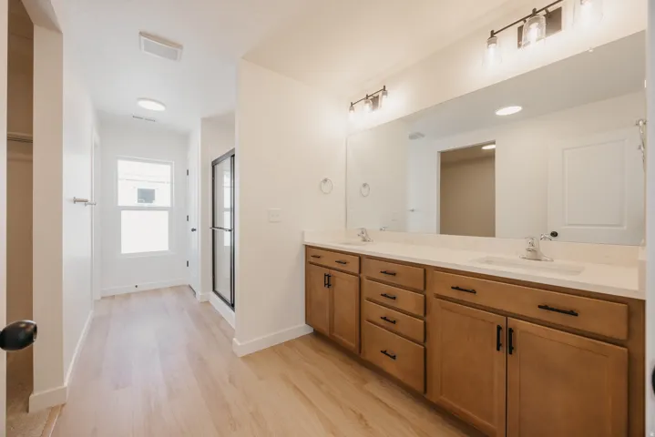 Bathroom featuring a dual vanity with light-toned wood cabinetry, a white countertop, and a full-width mirror