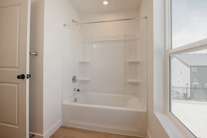 Bathroom featuring a white tub/shower combination with integrated shelving, chrome fixtures, a single recessed light, and wood-finish flooring