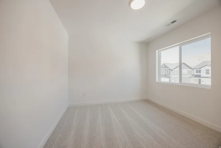 Bright room featuring a large window, neutral carpeting, and white baseboards