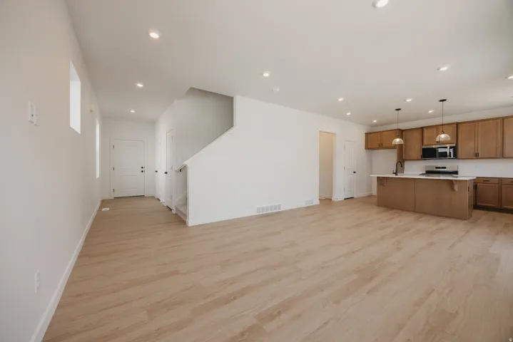 Spacious open-concept area featuring light wood-finish flooring, recessed lighting, and a modern kitchen