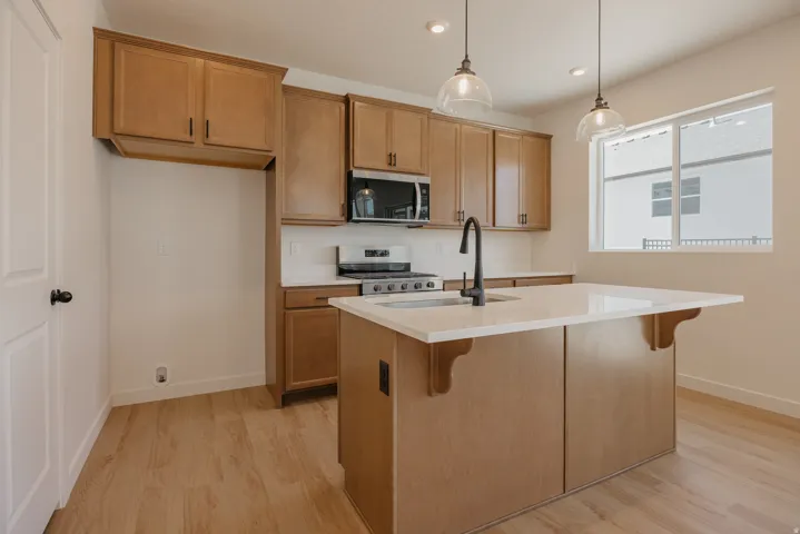 Open-concept kitchen featuring wood-finish flooring, light wood cabinetry, white subway tile backsplash, and a large window