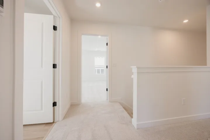 Upper-level hallway featuring a carpeted floor, recessed lighting, and a white paneled door with black hardware