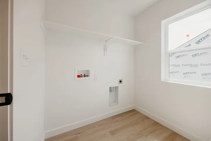 Dedicated utility room featuring light wood-finish flooring, a white fixed shelving unit, and a window with white trim