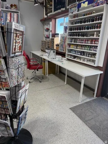 Expansive workspace featuring white laminate countertops, a large window, built-in shelving, track lighting, and speckled flooring