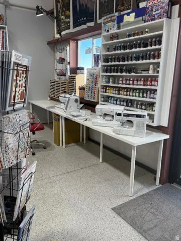 Spacious work area featuring durable terrazzo flooring, ample natural light from a prominent window, extensive built-in shelving, and a wall-mounted task light