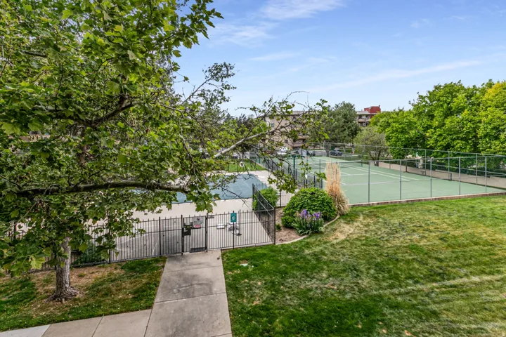 Spacious outdoor area featuring a tennis court with chain-link fencing, a second court, and surrounding green space