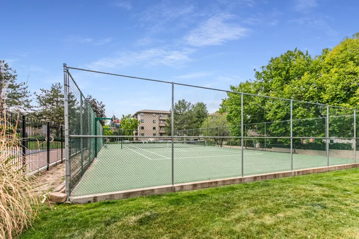 Fenced tennis court with a green playing surface and white court lines