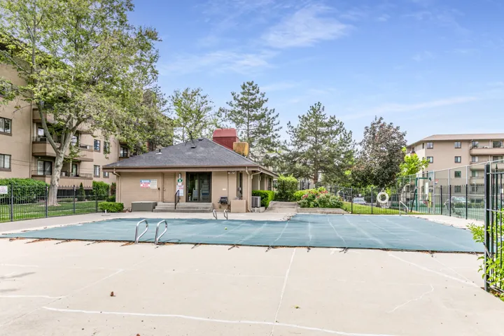 Outdoor pool with a protective cover, surrounded by a concrete deck and a black metal fence