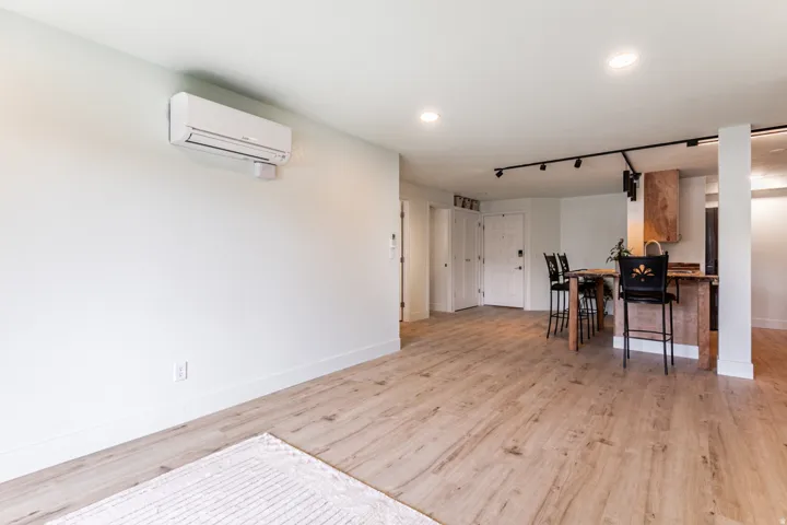 Open-concept living area featuring wood-finish flooring, a wall-mounted mini-split system, recessed lighting, and track lighting