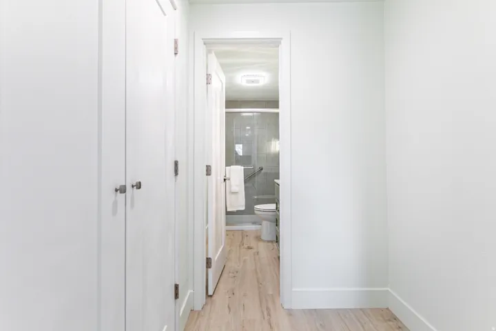 Recessed lighting illuminates a bathroom with a glass-enclosed shower, wall-mounted grab bars, and a white toilet