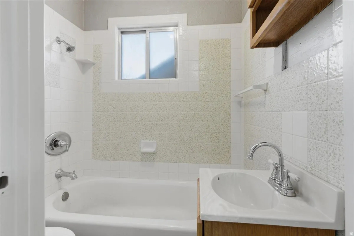 Bathroom featuring a white bathtub with chrome fixtures, a sliding window, and tiled walls