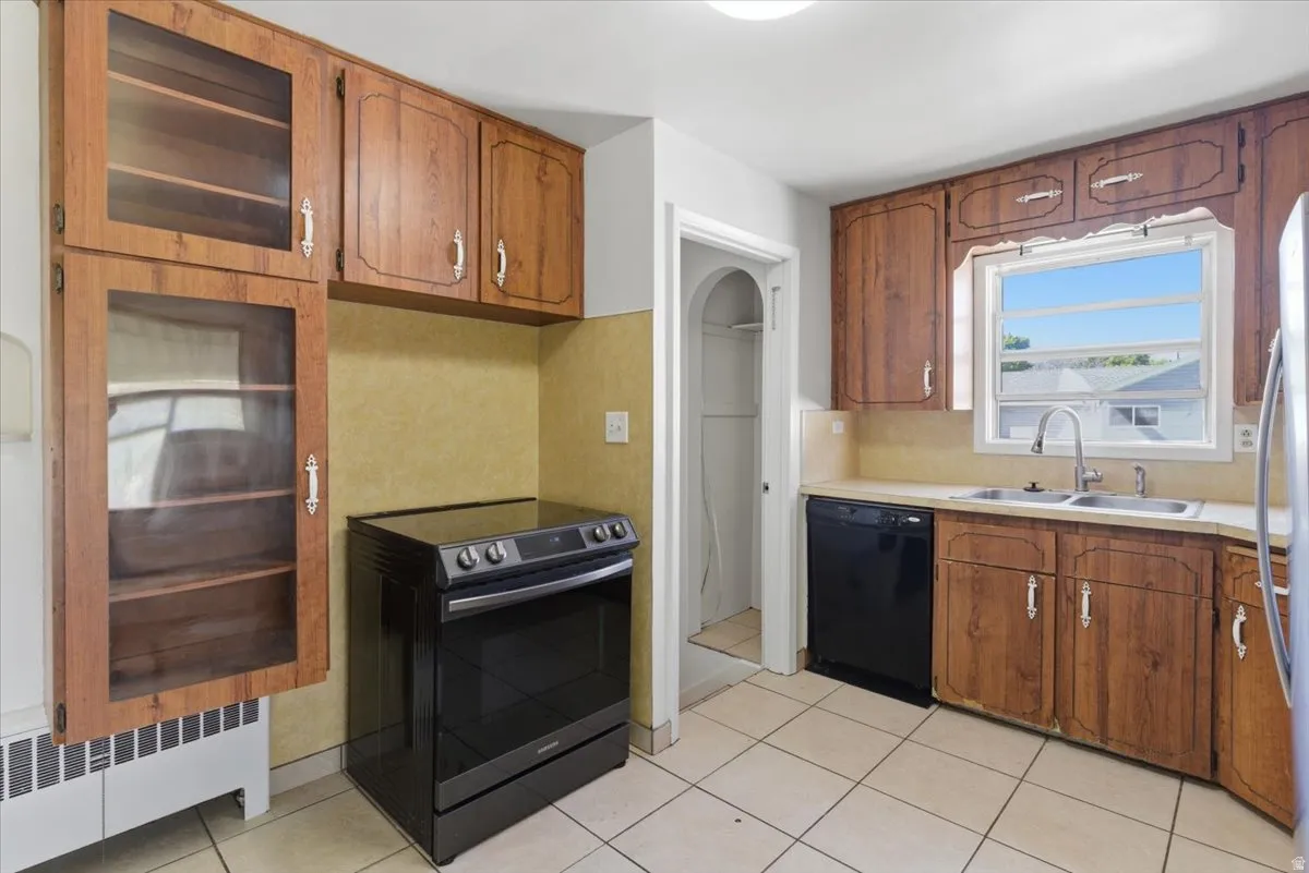 Kitchen featuring wood-finish cabinetry, a black electric range, a double basin sink, and a black dishwasher