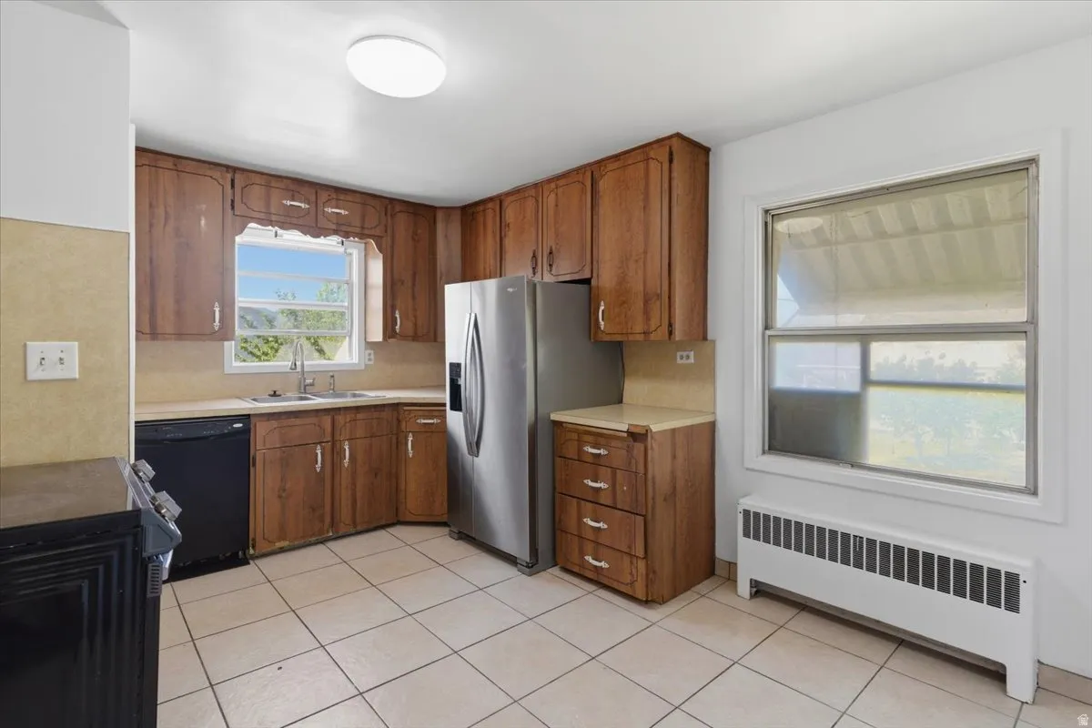 Kitchen featuring wood cabinetry, stainless steel refrigerator, black dishwasher, and tiled flooring
