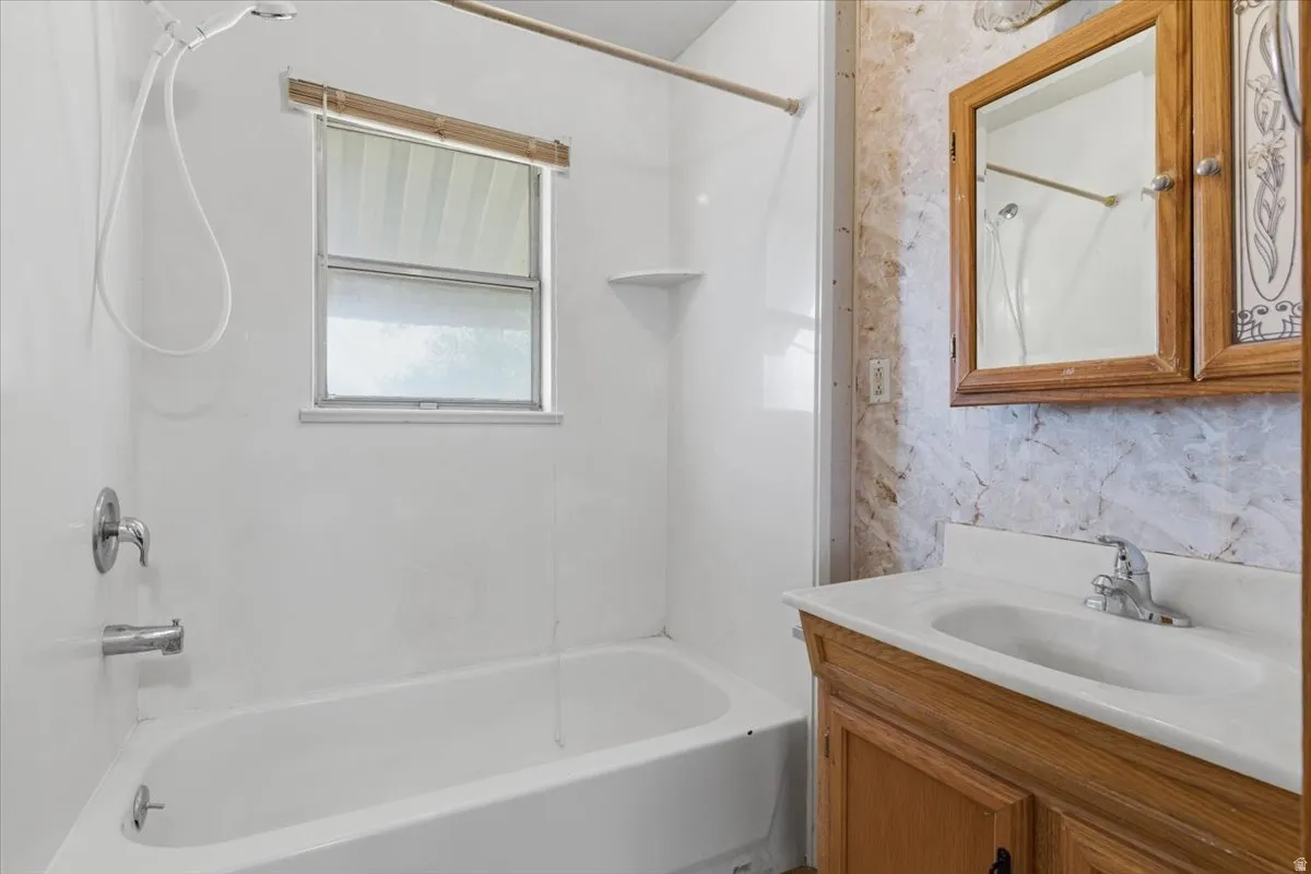 Bathroom featuring a white tub, shower with chrome fixtures, a window with blinds, a wood-finish vanity with a white countertop, and a mirrored medicine cabinet